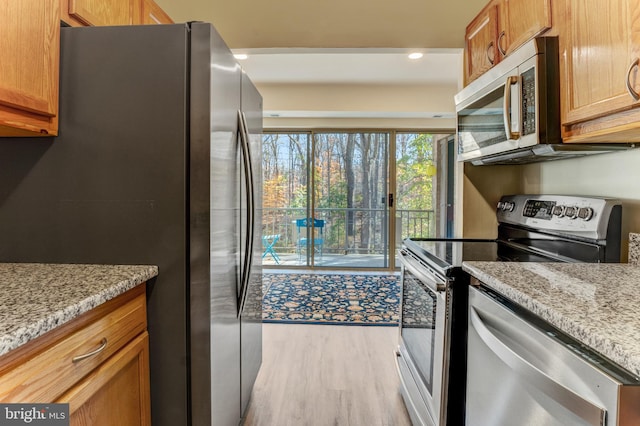 kitchen featuring light stone countertops, appliances with stainless steel finishes, and light wood-type flooring