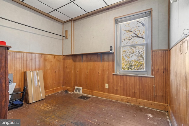 empty room featuring dark wood-type flooring, wood walls, and a drop ceiling