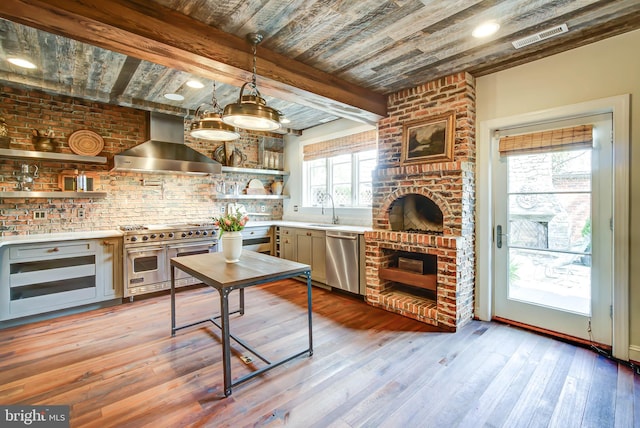 kitchen featuring wall chimney range hood, appliances with stainless steel finishes, sink, beamed ceiling, and light hardwood / wood-style flooring