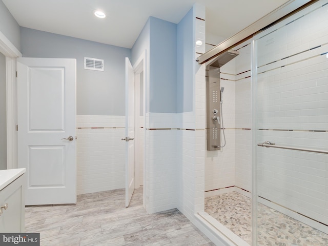 bathroom featuring walk in shower, vanity, and tile walls