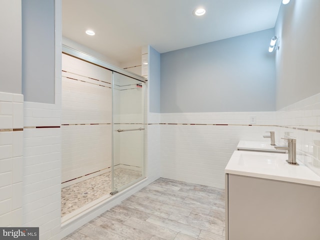 bathroom with hardwood / wood-style flooring, a shower with shower door, vanity, and tile walls