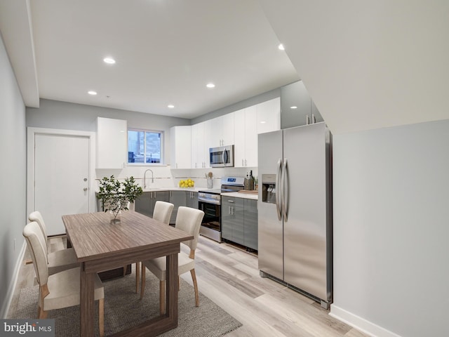 kitchen with stainless steel appliances, white cabinets, sink, and light wood-type flooring