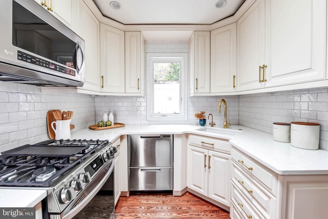 kitchen with stainless steel appliances, backsplash, light stone countertops, sink, and hardwood / wood-style flooring