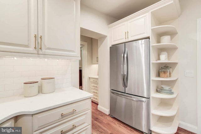 kitchen featuring white cabinets, light wood-type flooring, backsplash, and stainless steel fridge