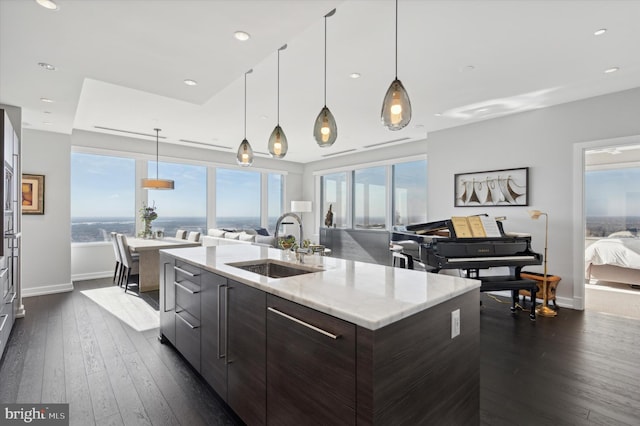 kitchen with dark brown cabinetry, hanging light fixtures, sink, an island with sink, and dark wood-type flooring