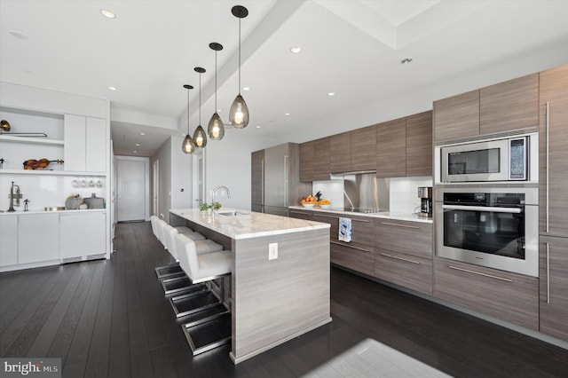 kitchen with a center island with sink, stainless steel appliances, sink, a breakfast bar area, and dark wood-type flooring