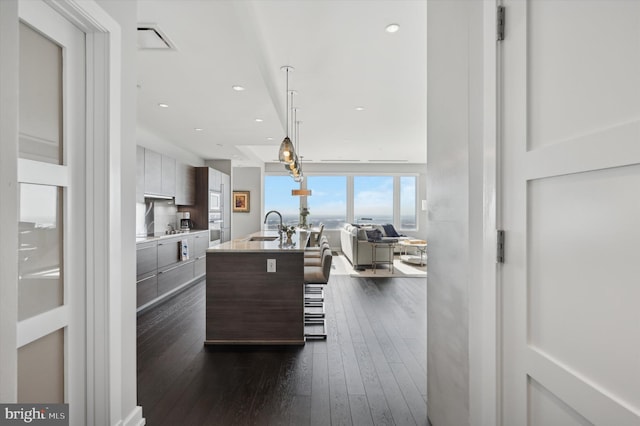 kitchen with dark brown cabinetry, sink, an island with sink, pendant lighting, and dark hardwood / wood-style flooring