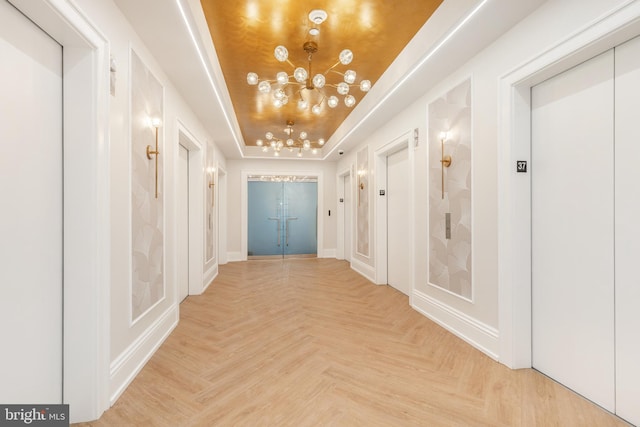 hallway with elevator, a raised ceiling, and light parquet flooring