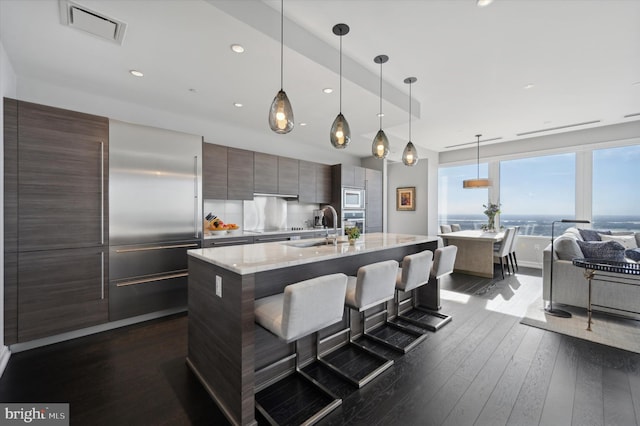 kitchen with dark wood-type flooring, a breakfast bar area, sink, an island with sink, and decorative light fixtures