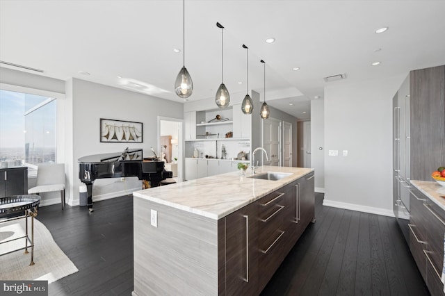 kitchen with sink, light stone countertops, an island with sink, dark brown cabinets, and dark hardwood / wood-style flooring