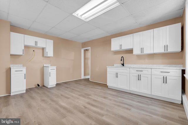 kitchen featuring sink, white cabinets, a drop ceiling, and light hardwood / wood-style flooring