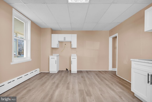 unfurnished living room with a baseboard radiator, a drop ceiling, and light hardwood / wood-style floors