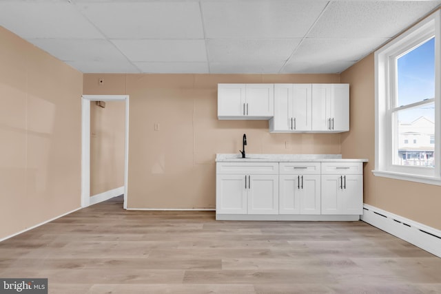 interior space featuring white cabinetry, sink, light hardwood / wood-style floors, and a drop ceiling