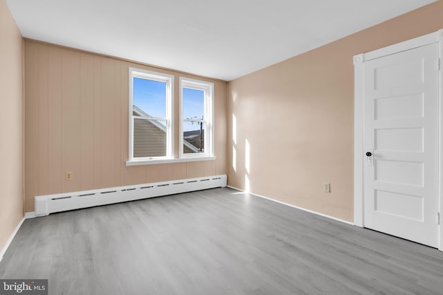 empty room featuring light hardwood / wood-style floors, a baseboard heating unit, and wood walls