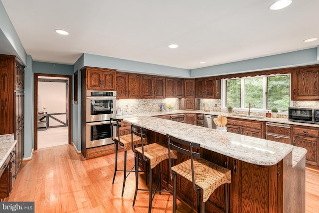 kitchen with sink, appliances with stainless steel finishes, a kitchen bar, light hardwood / wood-style flooring, and a kitchen island