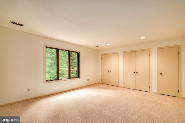 unfurnished bedroom with multiple closets and light carpet