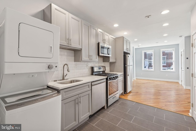 kitchen with dark wood-type flooring, stacked washer and dryer, sink, decorative backsplash, and appliances with stainless steel finishes