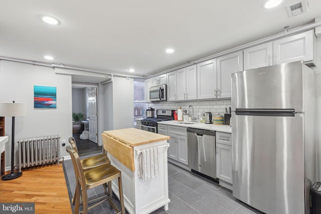 kitchen with radiator, sink, decorative backsplash, wood-type flooring, and stainless steel appliances