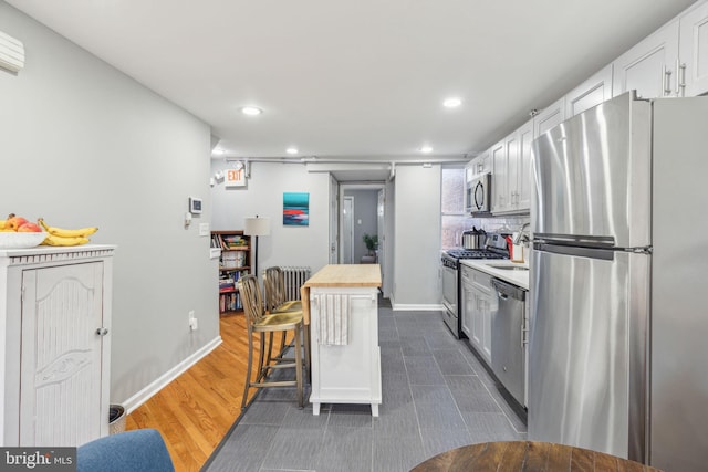 kitchen with wood counters, appliances with stainless steel finishes, a breakfast bar, dark wood-type flooring, and white cabinetry