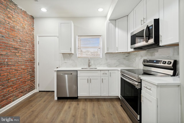 kitchen with white cabinetry, appliances with stainless steel finishes, brick wall, and sink