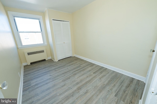 unfurnished bedroom with a closet, radiator heating unit, and light hardwood / wood-style flooring