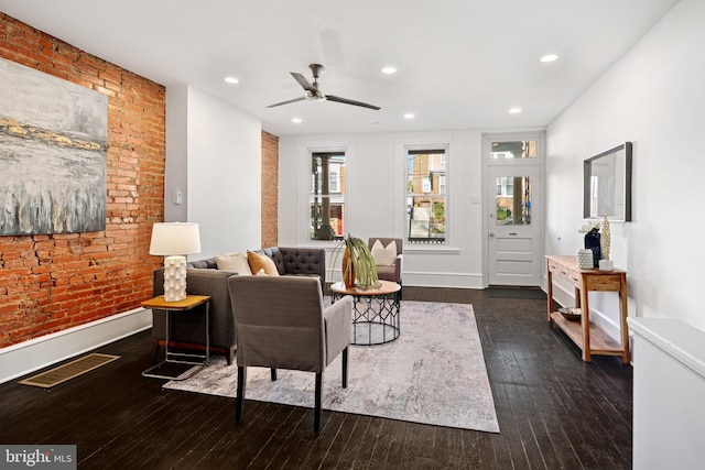 living room with ceiling fan, dark hardwood / wood-style flooring, and brick wall