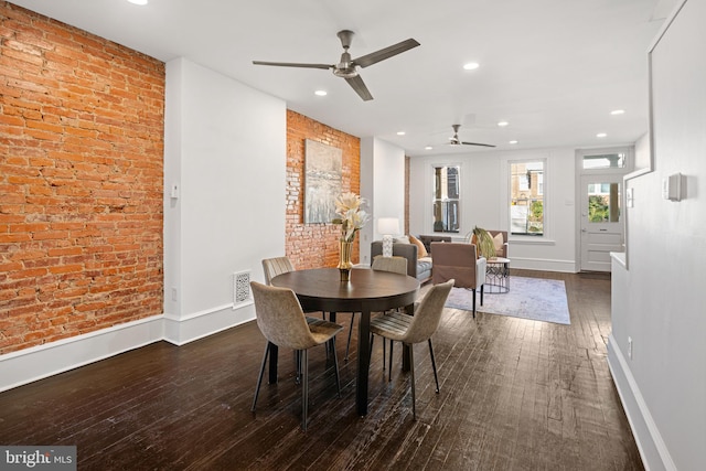 dining room featuring ceiling fan, dark wood-type flooring, and brick wall