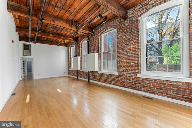 interior space with beam ceiling, light wood-type flooring, and brick wall