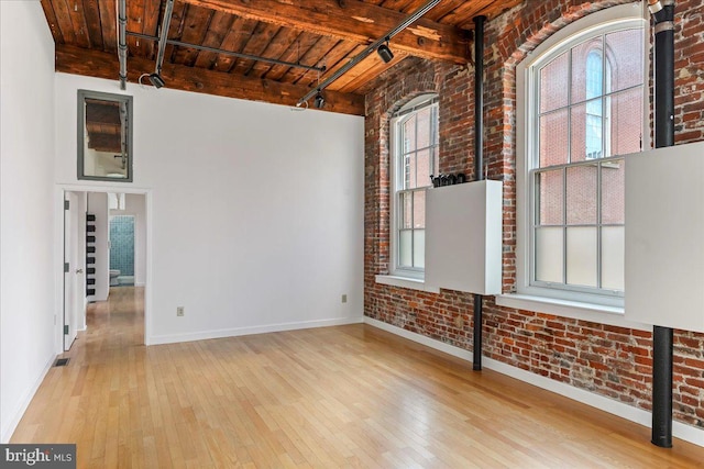 spare room featuring beam ceiling, wooden ceiling, light hardwood / wood-style flooring, and brick wall