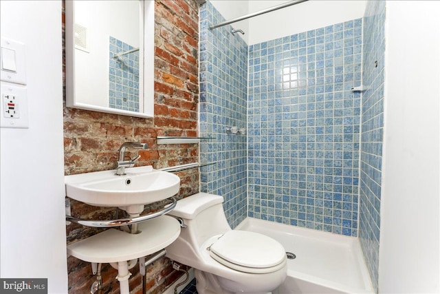 bathroom featuring a tile shower, sink, brick wall, and toilet