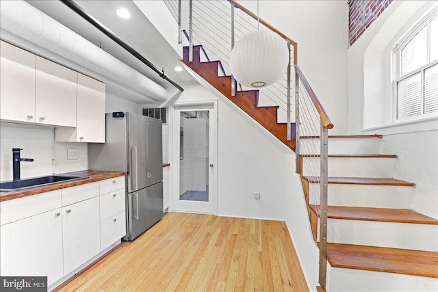 kitchen with light wood-type flooring, white cabinetry, hanging light fixtures, and sink