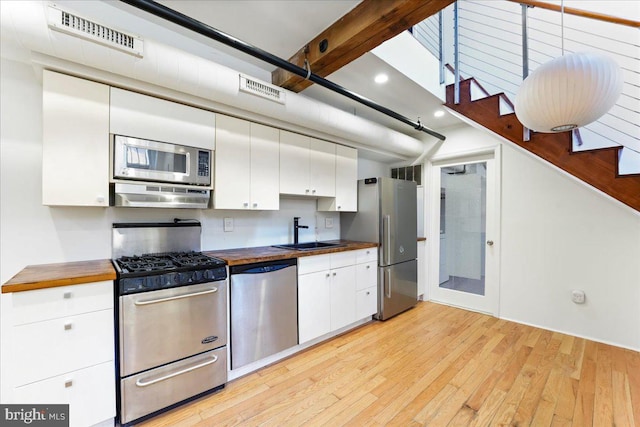 kitchen with butcher block countertops, sink, stainless steel appliances, and light hardwood / wood-style flooring