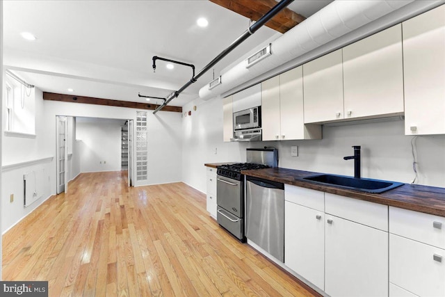 kitchen with stainless steel appliances, sink, light hardwood / wood-style floors, white cabinetry, and butcher block counters