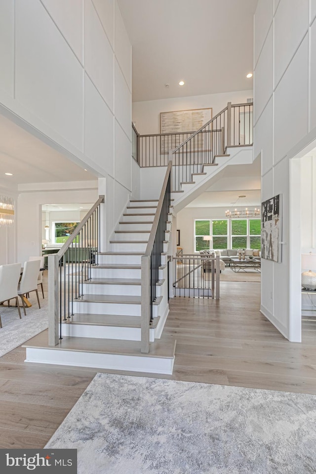stairway with wood finished floors, a high ceiling, recessed lighting, and a chandelier