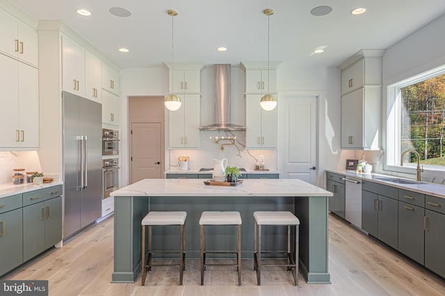 kitchen with wall chimney range hood, a sink, appliances with stainless steel finishes, light wood-style flooring, and decorative backsplash