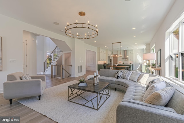 living area with a chandelier, light wood-type flooring, stairs, baseboards, and recessed lighting