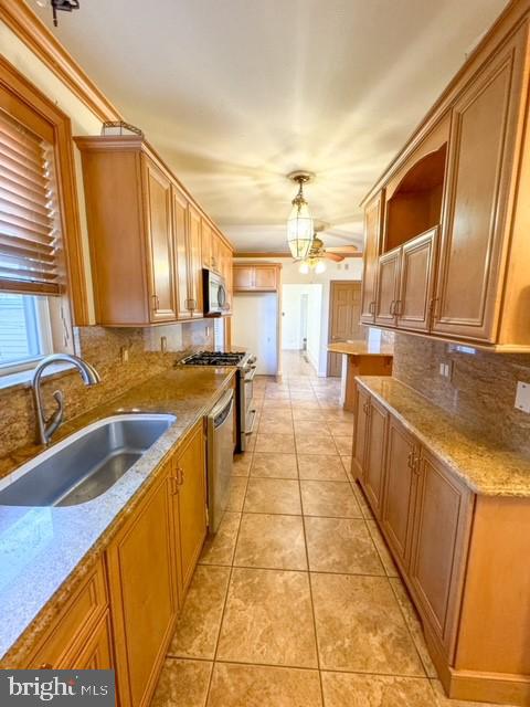 kitchen featuring light stone counters, decorative backsplash, sink, pendant lighting, and appliances with stainless steel finishes