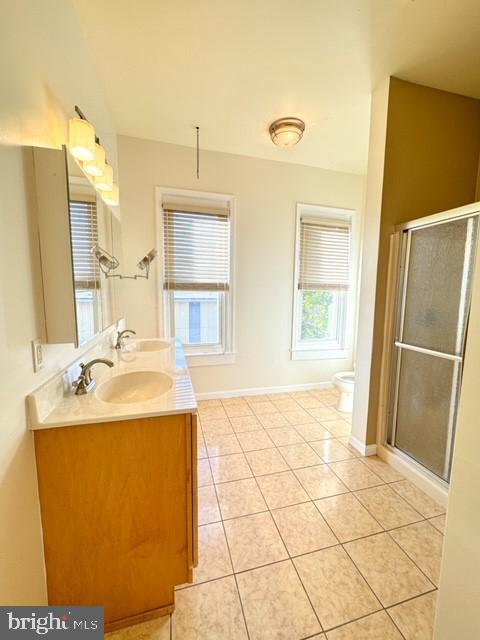 bathroom with toilet, plenty of natural light, tile patterned floors, and a shower with door