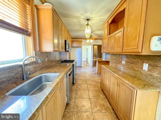 kitchen with stainless steel appliances, sink, light stone counters, light tile patterned floors, and hanging light fixtures