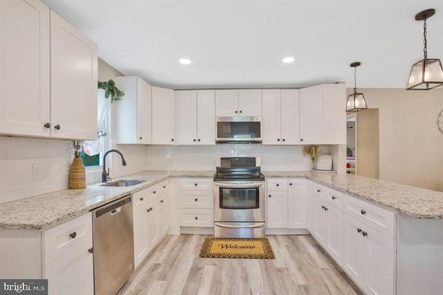 kitchen with appliances with stainless steel finishes, light wood-type flooring, sink, decorative light fixtures, and white cabinetry