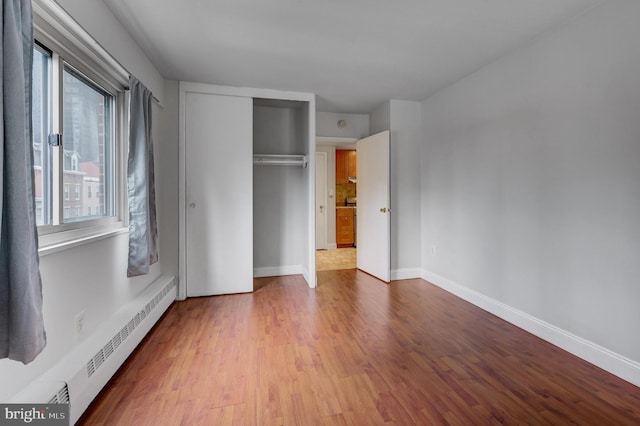 unfurnished bedroom featuring a closet, light hardwood / wood-style flooring, and a baseboard heating unit