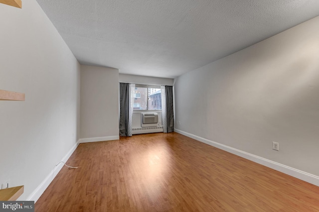 unfurnished room featuring a wall mounted air conditioner, wood-type flooring, a textured ceiling, and baseboard heating