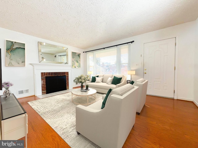 living room with light wood-type flooring, a textured ceiling, and a brick fireplace