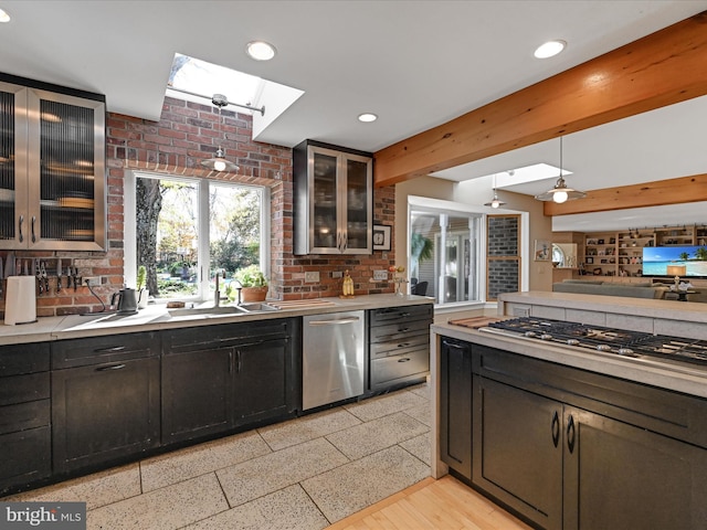 kitchen with appliances with stainless steel finishes, pendant lighting, sink, a skylight, and light hardwood / wood-style flooring