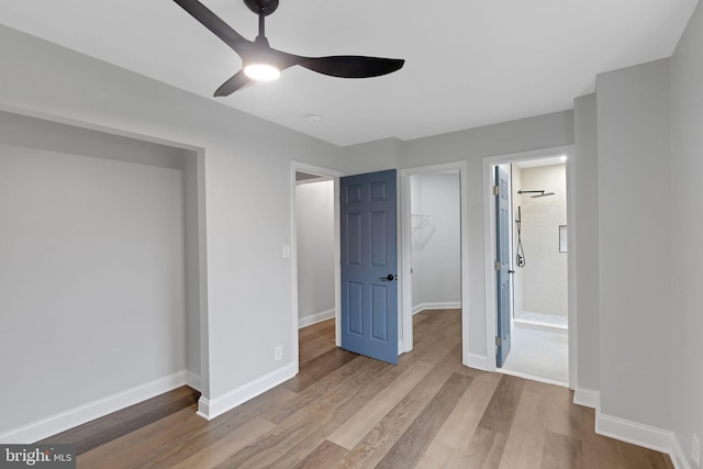 unfurnished bedroom featuring a walk in closet, light wood-type flooring, a closet, and ceiling fan