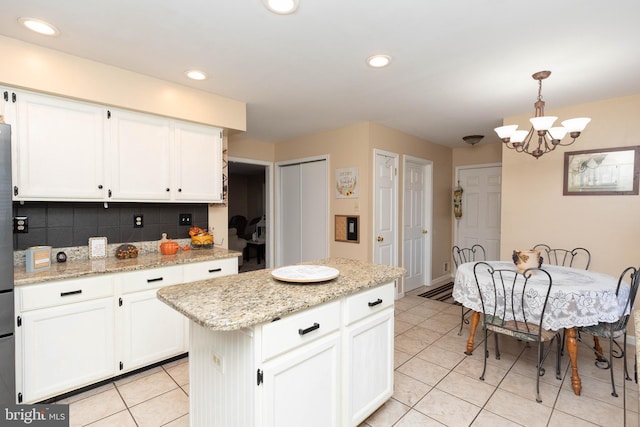 kitchen with light stone countertops, hanging light fixtures, a kitchen island, tasteful backsplash, and white cabinets