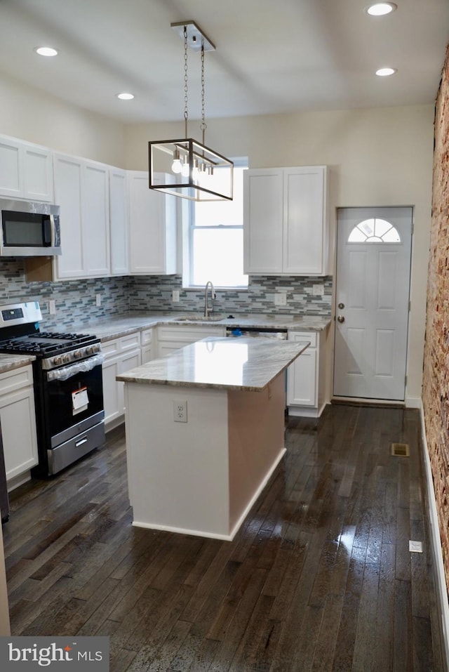 kitchen featuring white cabinetry, appliances with stainless steel finishes, hanging light fixtures, and a kitchen island