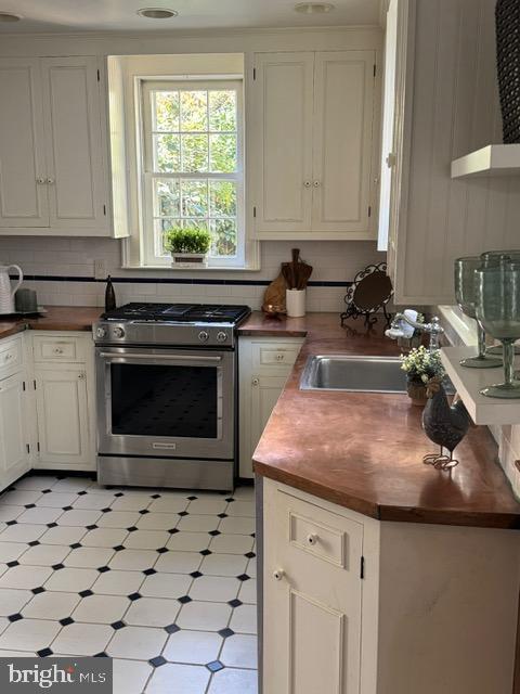 kitchen with backsplash, white cabinetry, sink, and gas range