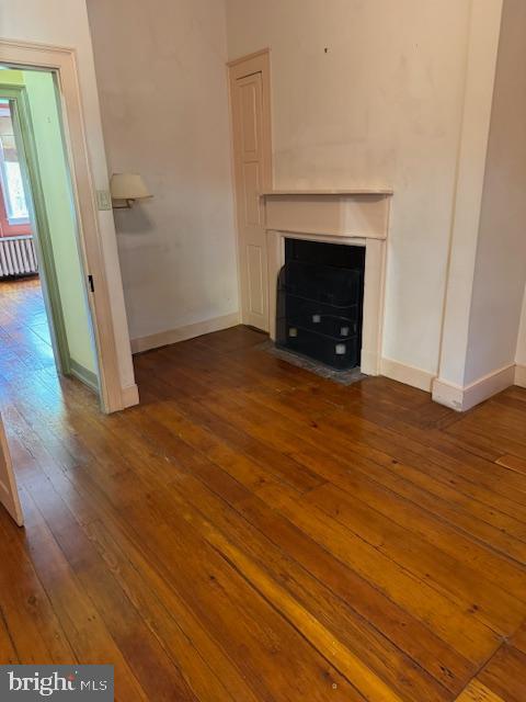 28 The Strand, New Castle, DE 19720 - unfurnished living room featuring a fireplace with flush hearth, hardwood / wood-style floors, baseboards, and radiator