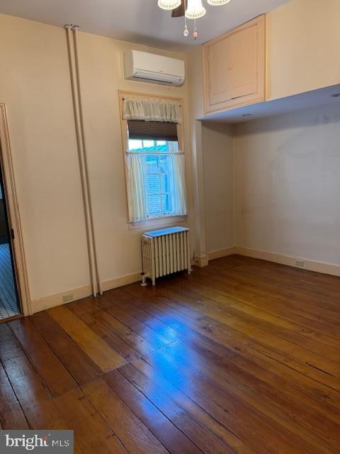 unfurnished room featuring radiator heating unit, a wall unit AC, and dark hardwood / wood-style floors